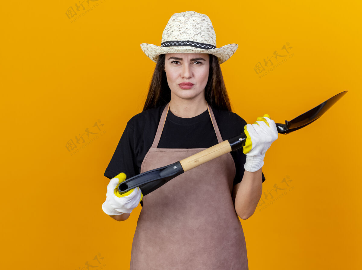 制服未出租美丽的园丁女孩穿着制服 戴着园艺帽子 手套拿着铁锹隔离在橙色背景上花园女孩手套