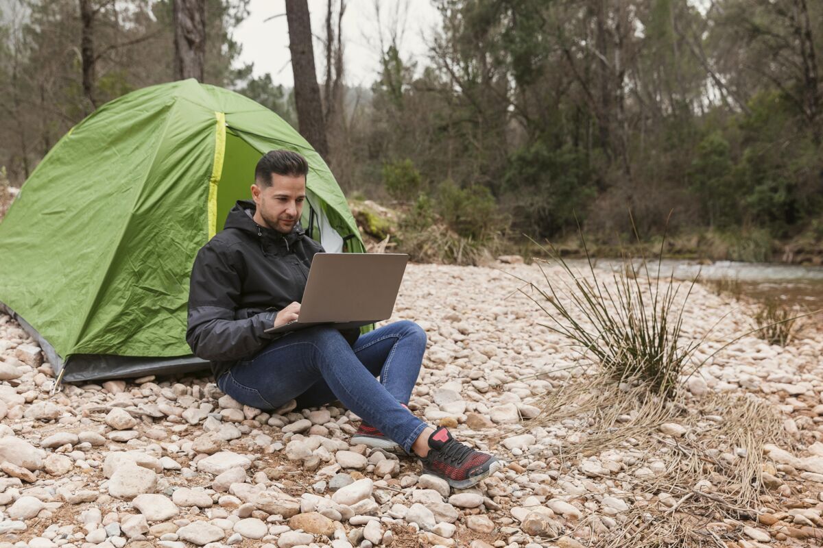 笔记本电脑帐篷旁的人拿着笔记本电脑探索自然露营