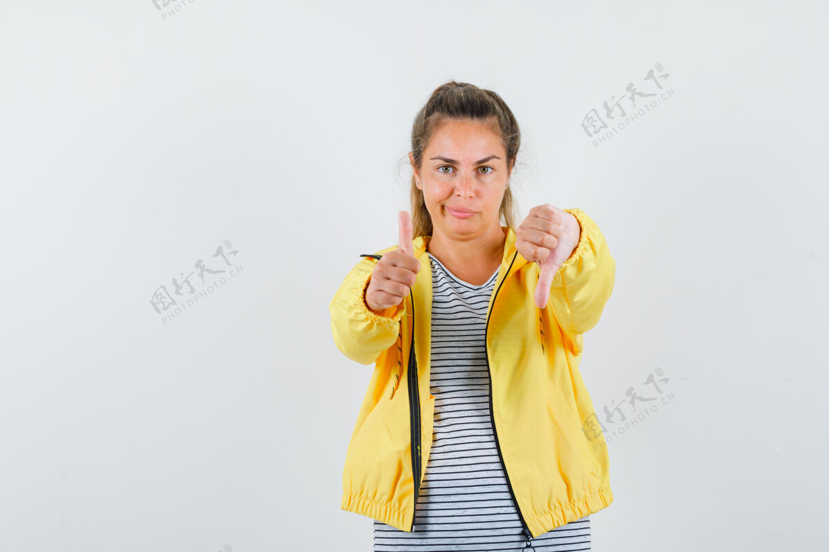 条纹一个金发女人 穿着黄色棒球服和条纹衬衫 上下竖起大拇指 做鬼脸 看上去很沉思头发衬衫人