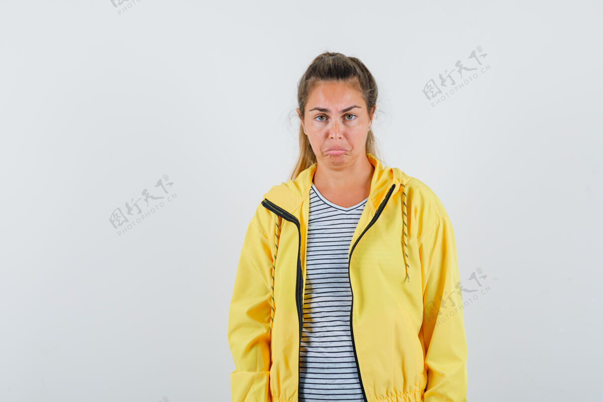护理穿着黄色棒球服和条纹衬衫的金发女人笔直地站着 做鬼脸 在镜头前摆姿势 看起来很漂亮快乐头发直