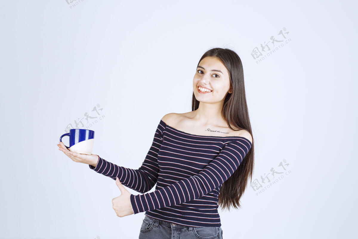 美食家穿着条纹衬衫的女孩拿着一个咖啡杯 展示着享受的标志姿势人体模特女人