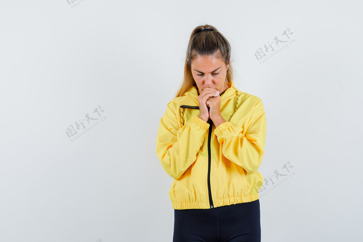 女性金发女人握紧拳头 站在祈祷姿势在黄色的棒球服夹克和黑色裤子 看起来专注成人站立干净