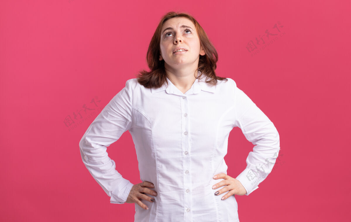 衬衫穿着白衬衫的年轻女子站在粉红色的墙上 看起来又累又无聊站着无聊疲倦