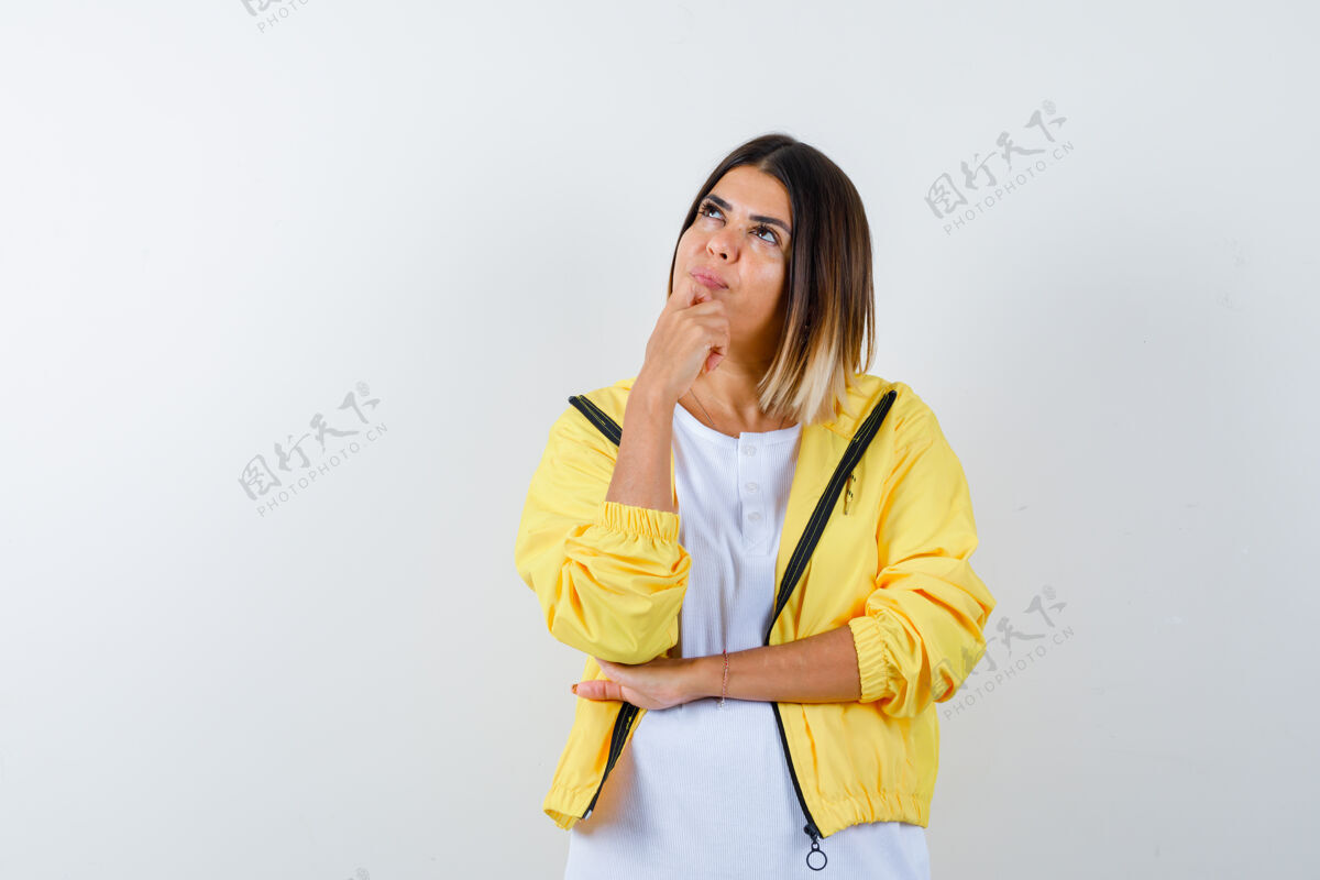 道具身穿白色t恤 黄色夹克的年轻女孩站在思考的姿势 手托下巴 神情沉思 俯视前方思考愉悦沉思