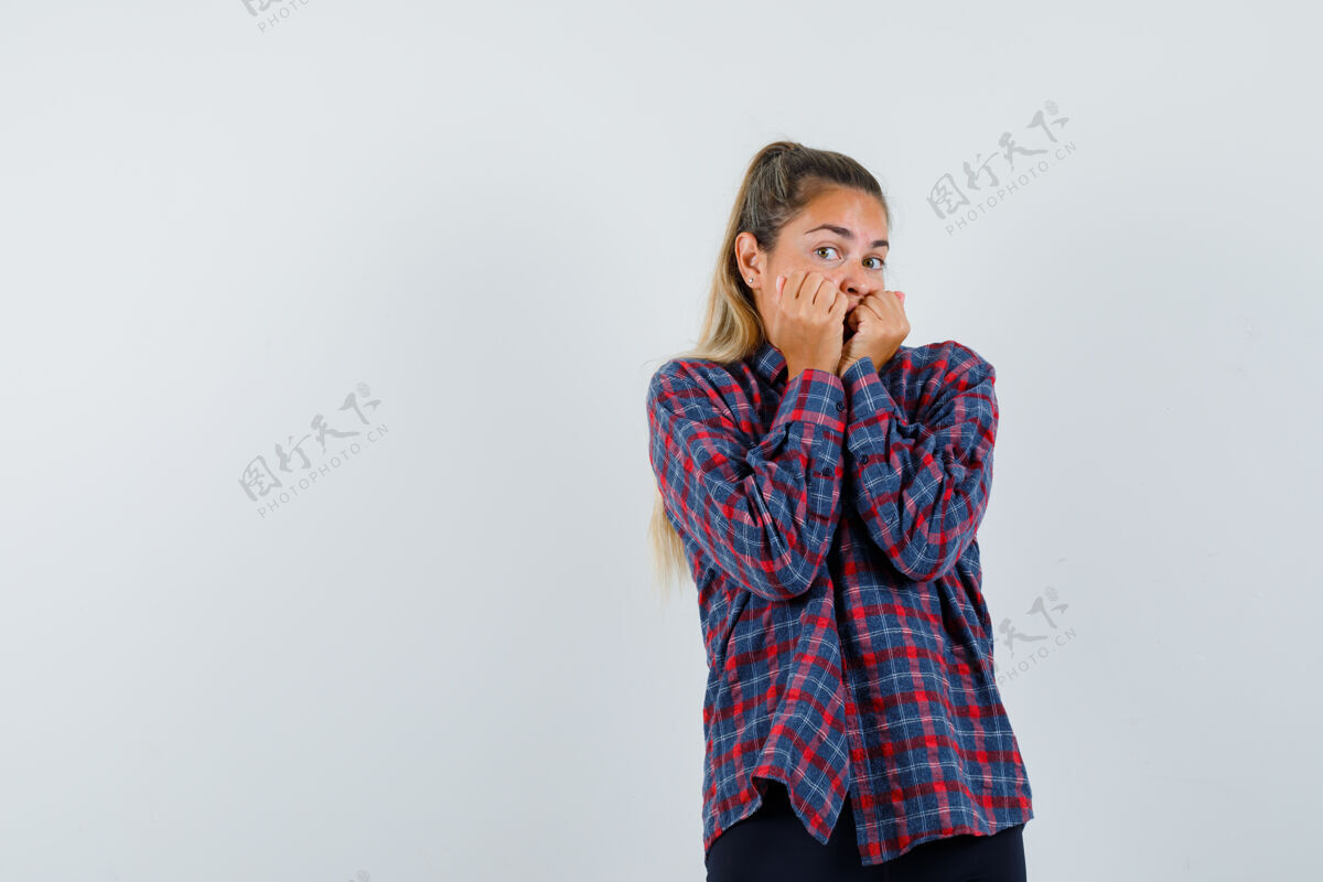 自然穿格子衬衫的年轻女子咬着拳头 看上去很害怕咬成人头发