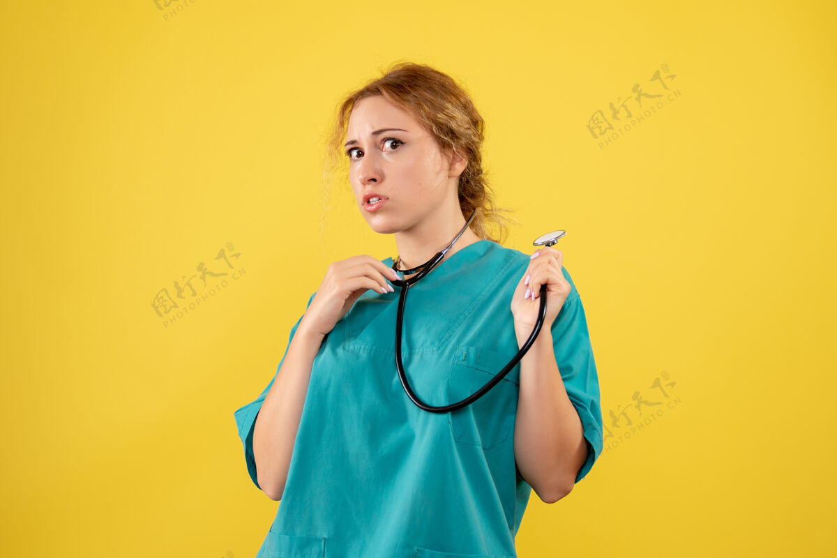 前面黄色墙壁上穿着带听诊器的医疗服的女医生的正视图情绪人女医生