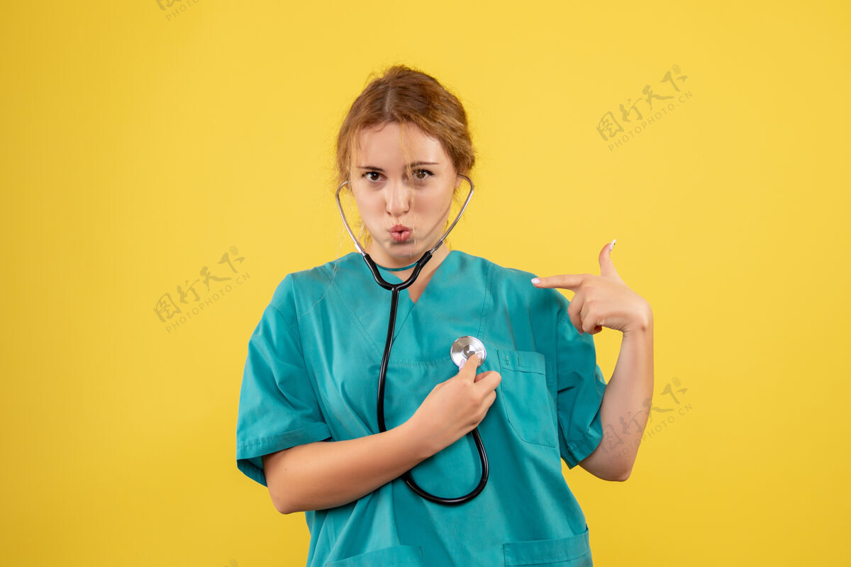 医疗器械黄色墙壁上穿着带听诊器的医疗服的女医生的正视图医疗医生病毒