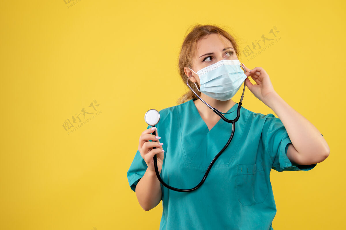 面罩黄墙上穿着医疗服 戴着听诊器面罩的女医生的正视图听诊器医疗仪器
