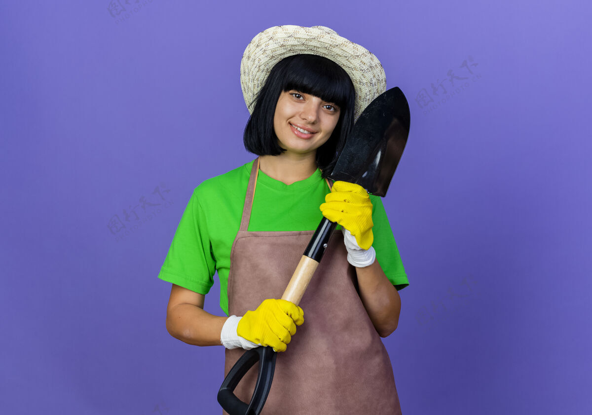 手套身着制服 戴着园艺帽和手套 手持铁锹 面带微笑的年轻女园丁年轻穿黑桃