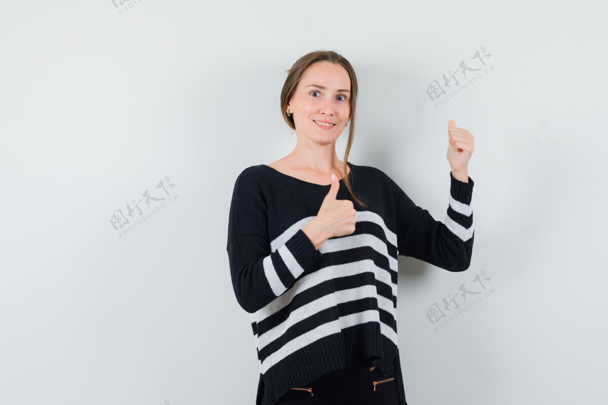 双人穿着条纹针织衫和黑色裤子的年轻女子竖起大拇指 看起来很开心模特护理干净