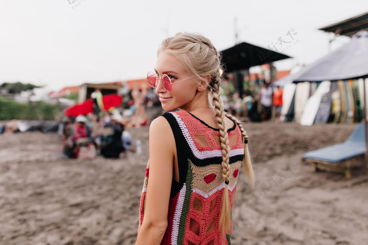 表情一个穿着针织背心的金发女人微笑着摆姿势的照片一个梳着辫子在沙滩上消磨时光的时髦女人的户外照片人度假头发