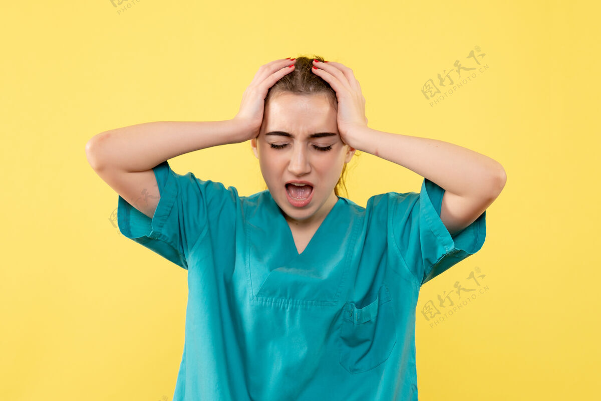 可爱黄色墙壁上穿着医疗服头痛的女医生的正视图模特女医生人