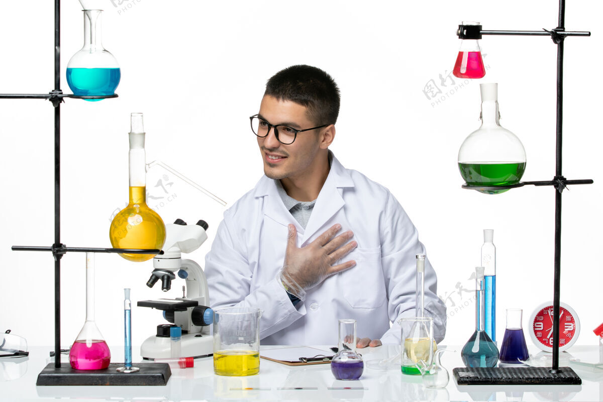 医院正面图：身穿医疗服的男性化学家坐在白色办公桌上 拿着解决方案病毒冠状病毒-疾病科学外套桌子病毒