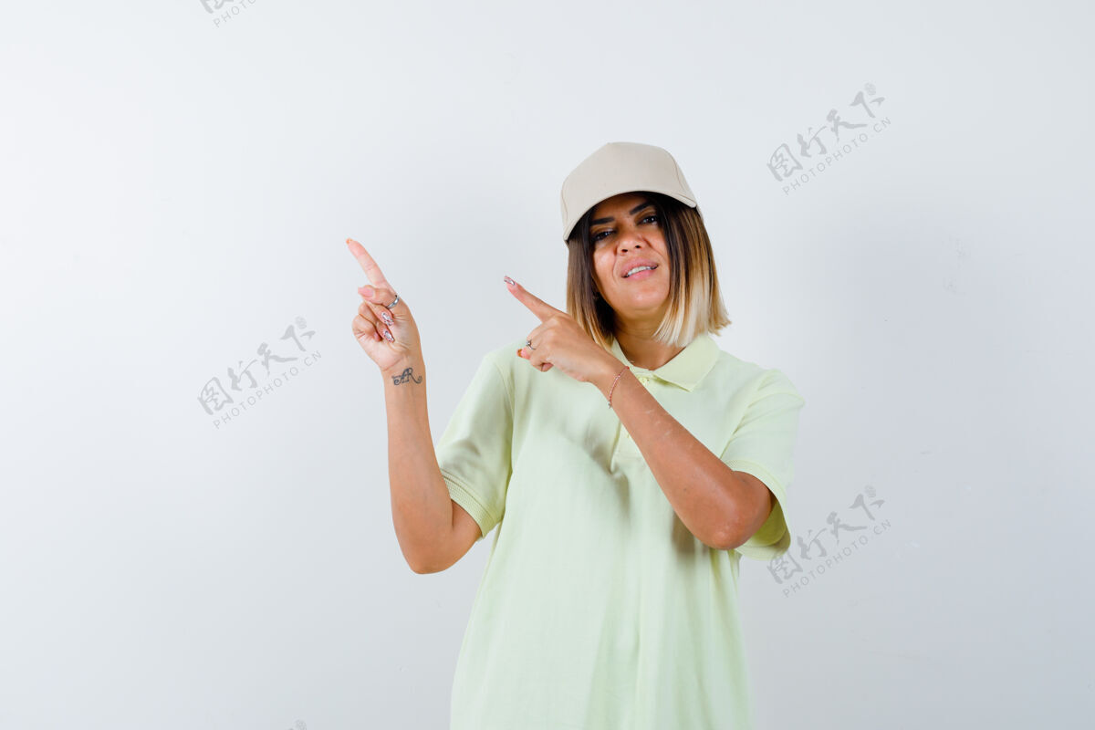 年轻年轻的女性指着左上角的t恤衫 戴着帽子 看上去兴高采烈 俯瞰前方时尚漂亮头