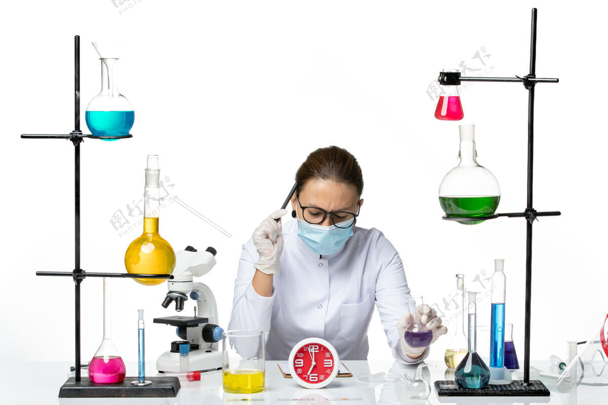 药品前视图穿着医疗服的女化学家戴着面罩坐着 拿着溶液 拿着钢笔 白色背景上的溶液溅起实验室病毒化学冠状病毒坐着化学钢笔