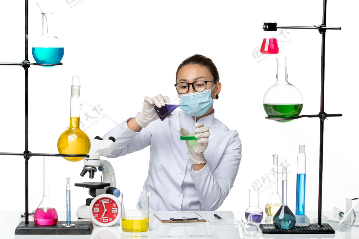 专业正面图：穿着医疗服的女化学家 戴着面罩 在白色地板上拿着不同的溶液 飞溅着病毒化学实验室的病毒实验室前面喷溅