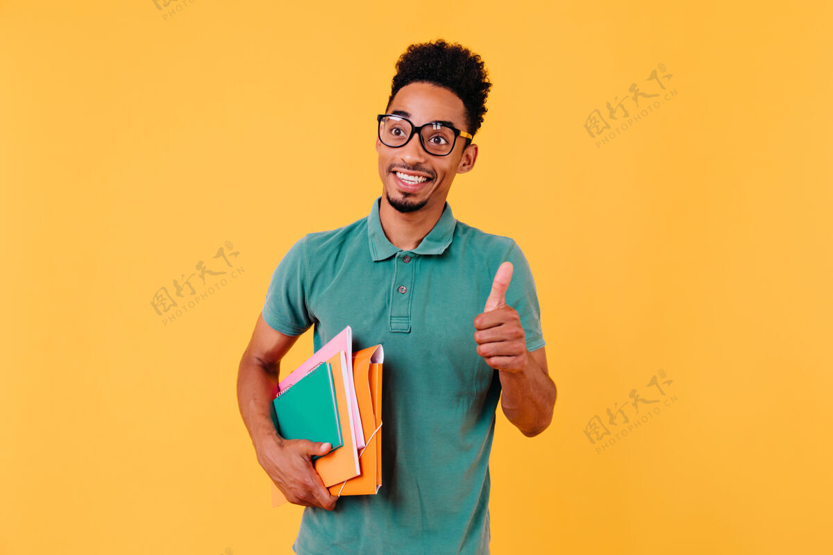 非洲兴奋的棕色头发的家伙戴着眼镜拿着书无忧无虑的非洲学生孤立了大学微笑可爱