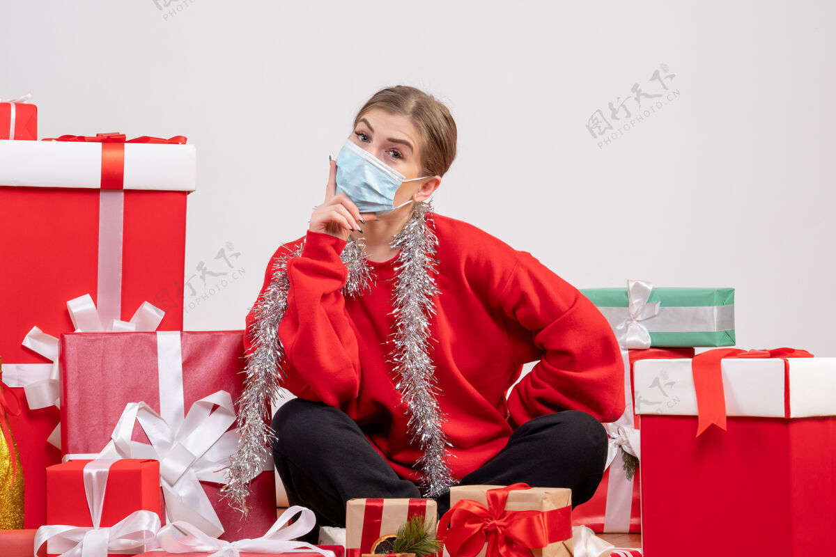 圣诞节正面图：年轻女性戴着无菌面具坐着 手里拿着圣诞礼物生活礼物坐着