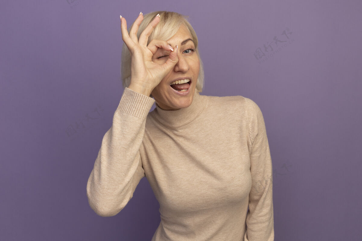 成年人快乐美丽的金发斯拉夫女人透过紫色的手指看着相机时尚斯拉夫姿势
