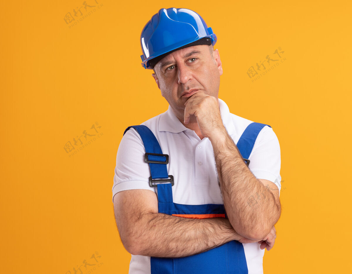 下巴体贴的白人成年建筑工人穿着制服 拿着下巴看着橙色的一边成年人思想人