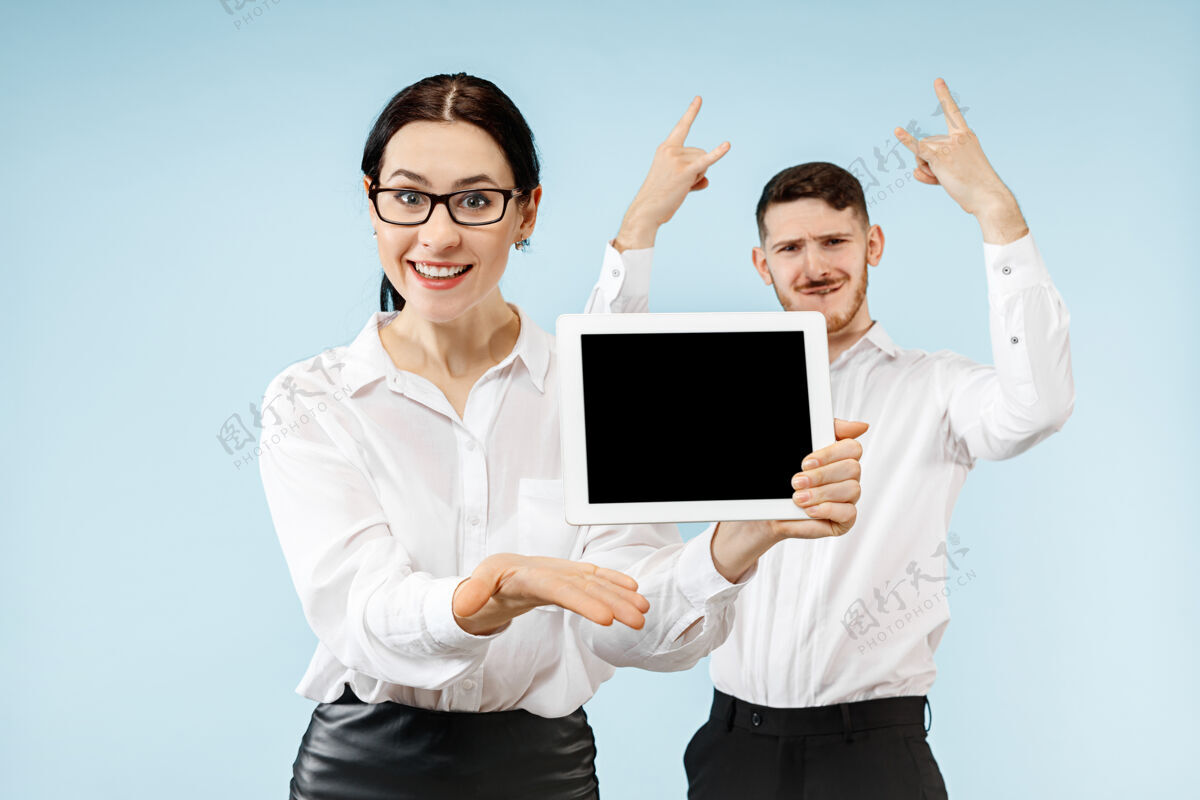 胜利惊讶的商人和女人在蓝色的工作室背景上微笑 展示笔记本电脑或平板电脑的空屏幕关系商业女人个人