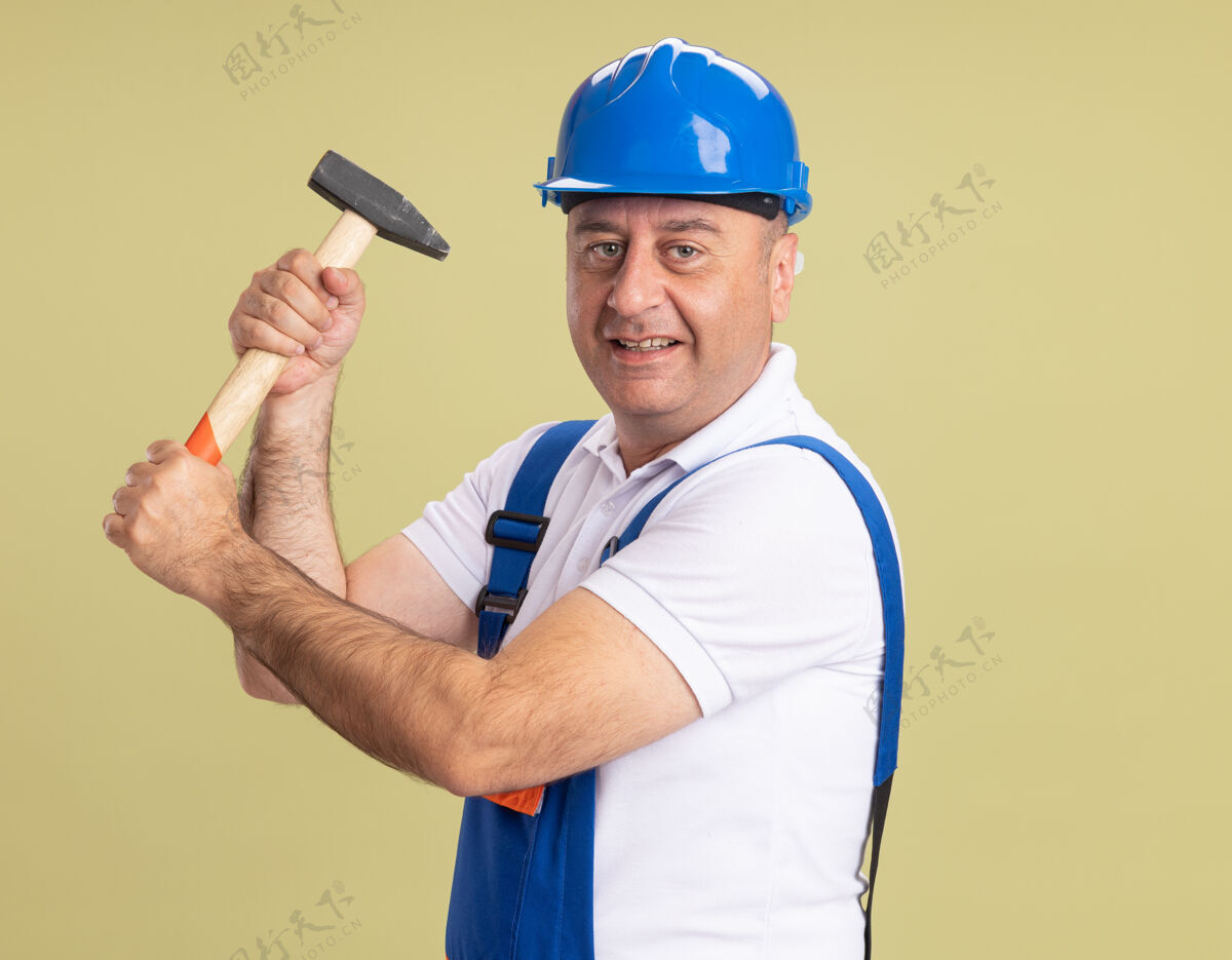 成年人身着制服的成年建筑工人微笑着拿着锤子敲打着橄榄绿人制服建筑工人