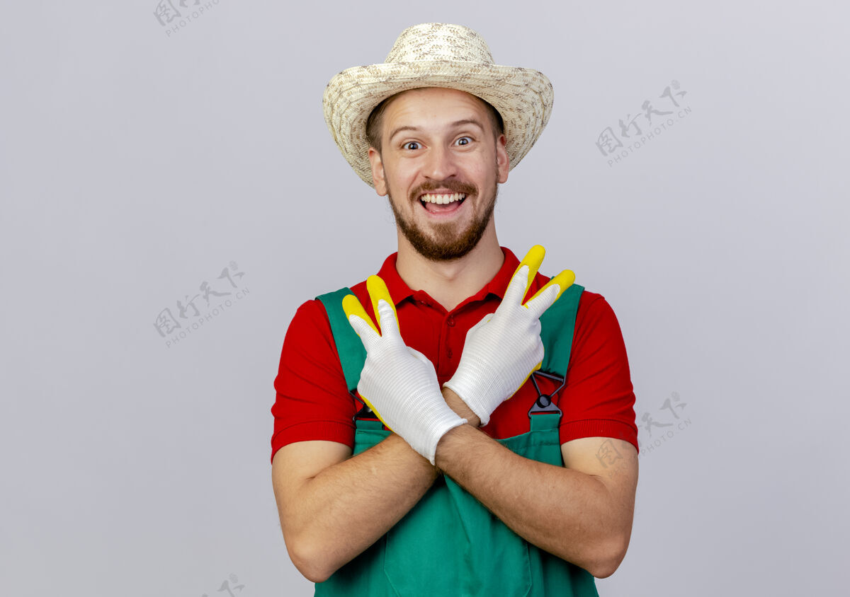 帽子快乐的年轻英俊的斯拉夫园丁穿着制服戴着园艺手套和帽子看着双手交叉做和平标志隔离和平人年轻