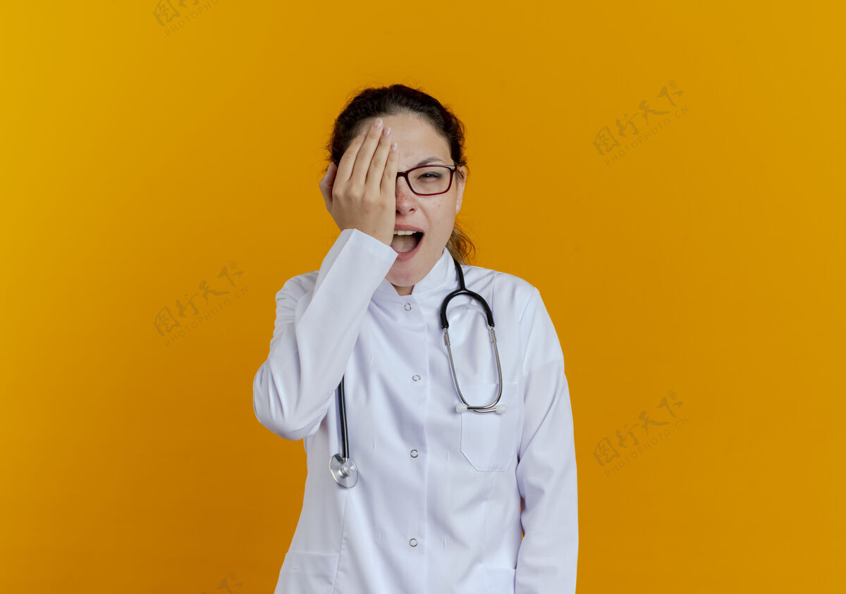 眼睛快乐的年轻女医生穿着医用长袍 戴着听诊器 戴着眼镜 手眼被隔离女人女人眼镜