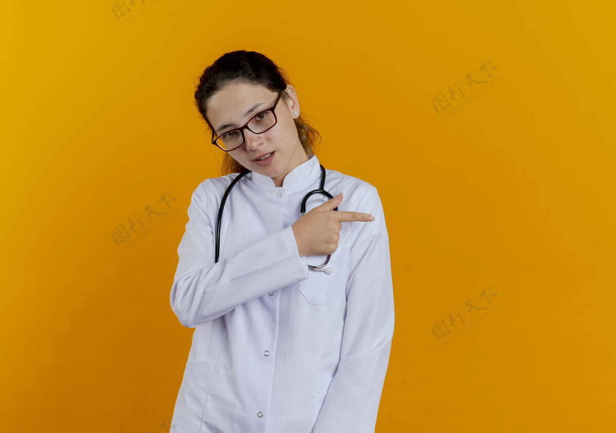 请高兴的年轻女医生穿着医用长袍和听诊器与眼镜点在一边隔离眼镜点穿