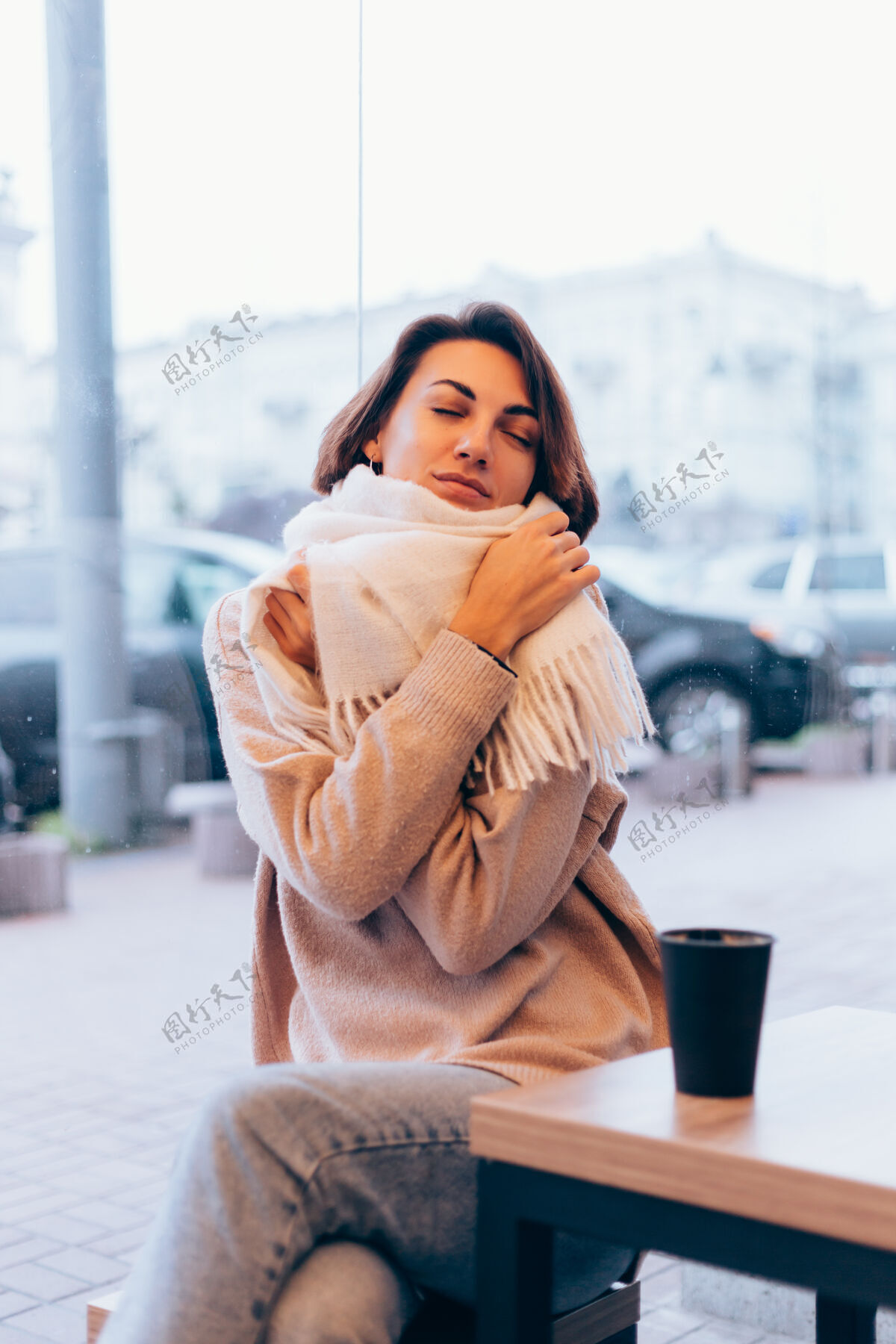 窗户一个女孩在舒适的咖啡馆里用一杯热咖啡取暖羊毛肖像女人