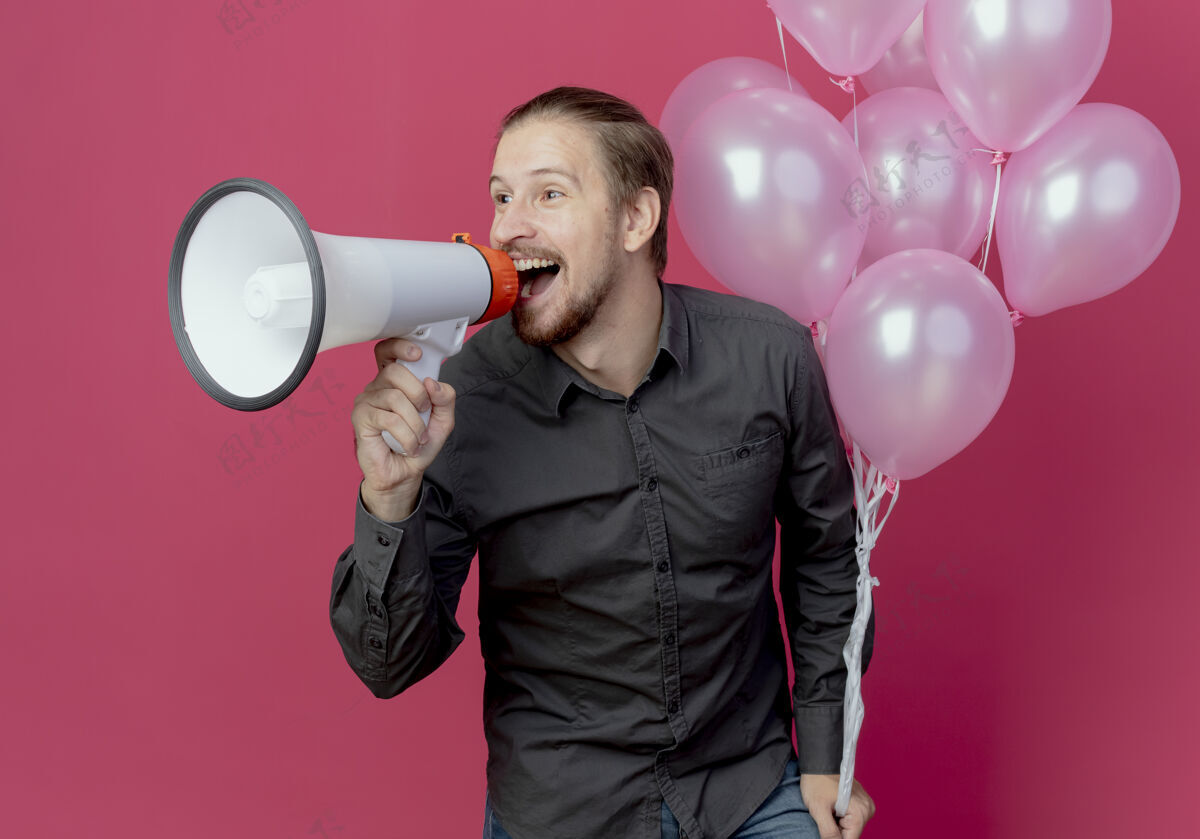 气球快乐的帅哥拿着氦气球站着 拿着扩音器 看着隔离在粉红色墙上的一面站着生日壁板