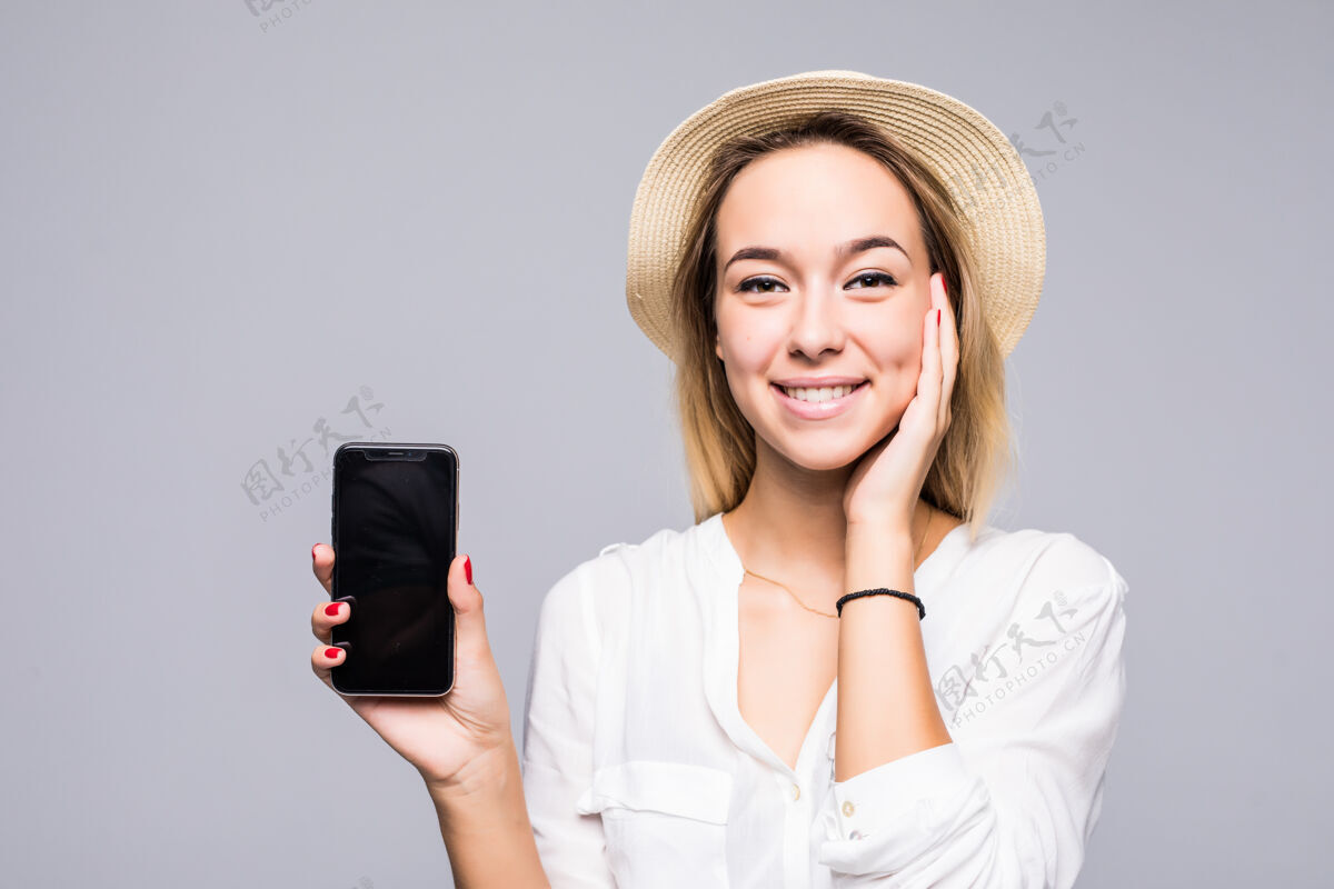 通话一个微笑的女人的特写肖像 在灰色的墙上孤零零地站着 展示着黑屏手机年轻手屏幕