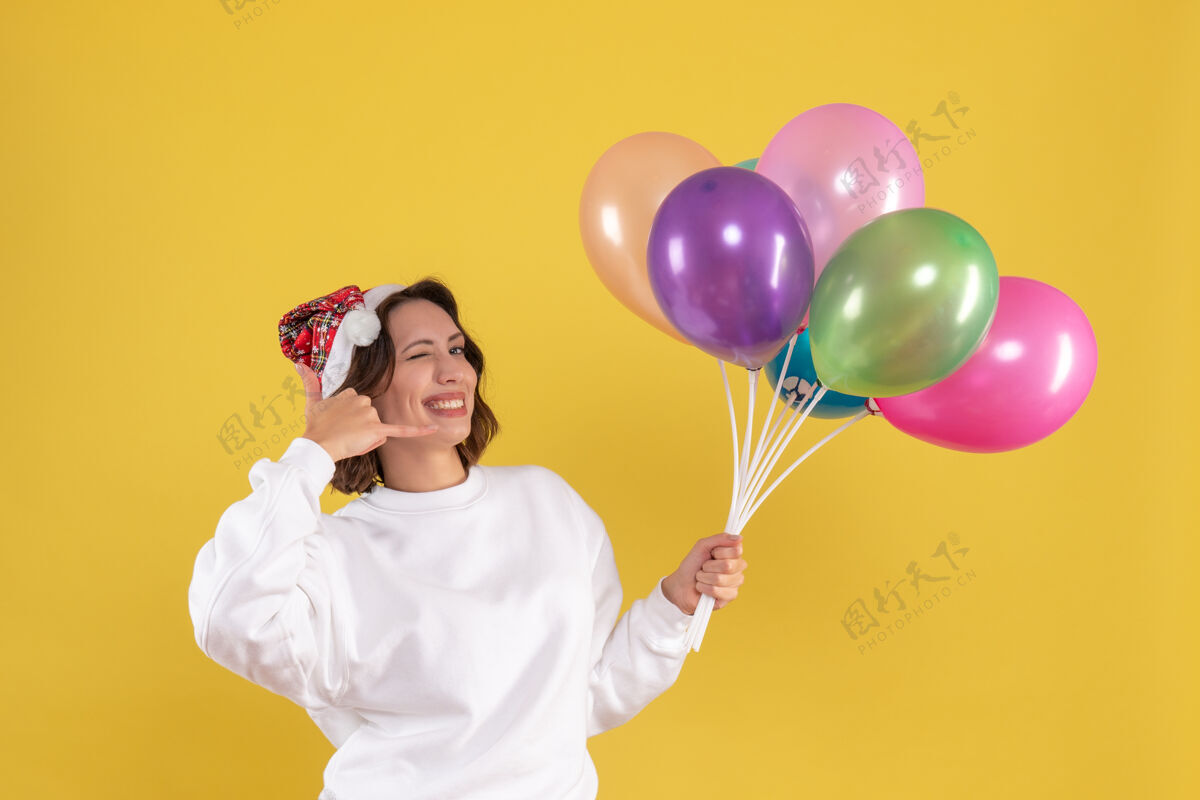 乐趣正面图漂亮的女人拿着五颜六色的气球在黄色的桌子上新年情感女人彩色圣诞氧气吹漂亮的女人