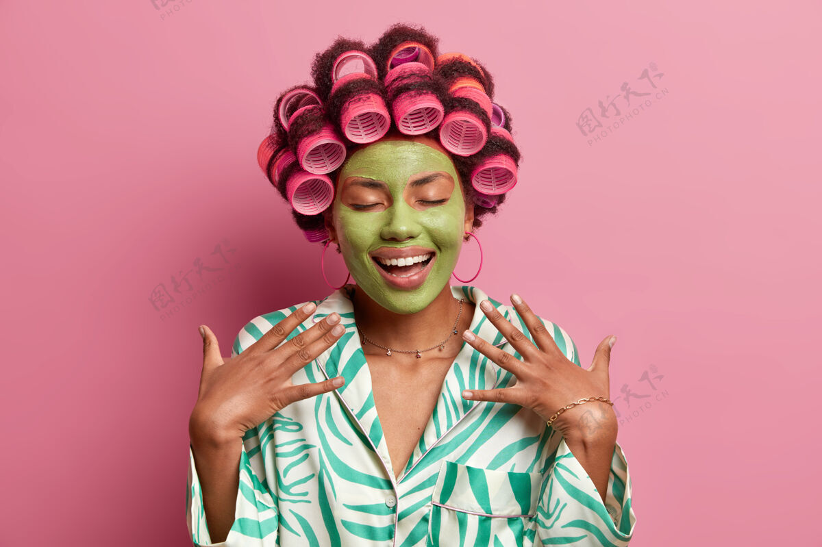 年轻快乐女士的肖像 带着健康皮肤的绿色美容面膜 闭上眼睛 梦想着在派对上有一个绝妙的造型 做一个完美的发型 穿着粉色的家常长袍心情家庭主妇面部