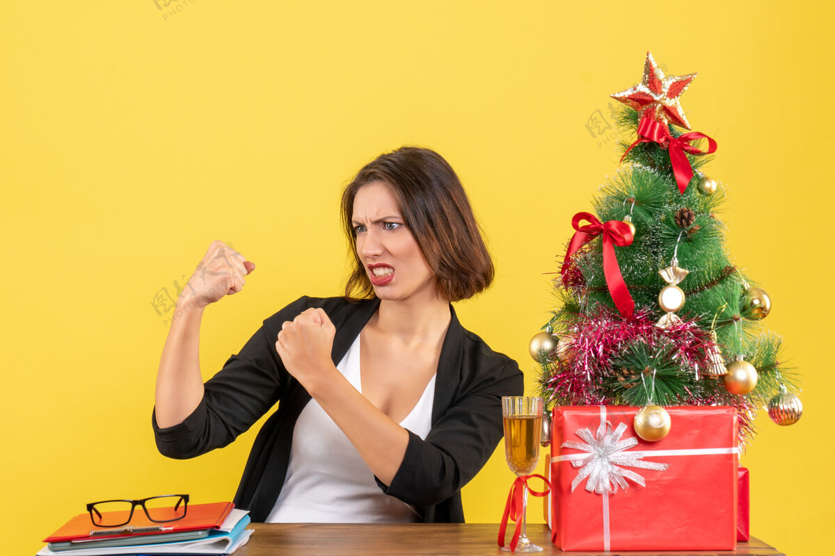快乐与坐在办公室桌子旁的年轻情绪化的商务女士共度圣诞节人欢呼人