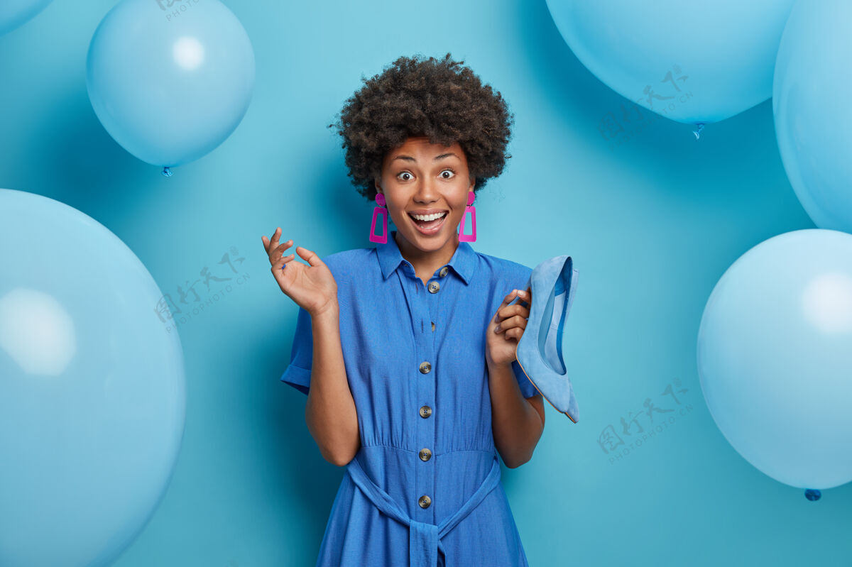氦快乐的时尚女士穿着蓝色的裙子 拿着高跟鞋来搭配她的服装 准备主题派对 买衣服 成为购物狂 孤立于装饰墙女人和风格时尚气球鞋子