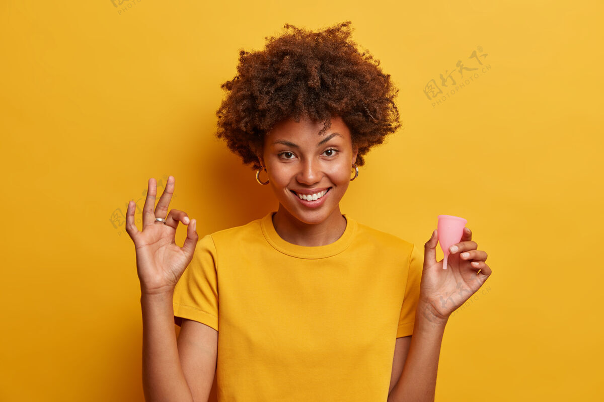 月经笑容可掬的美女赞成使用月经杯 做个好手势 手里拿着硅胶产品插入阴道 给女性推荐用黄色隔离杯的用户流体妇科卫生