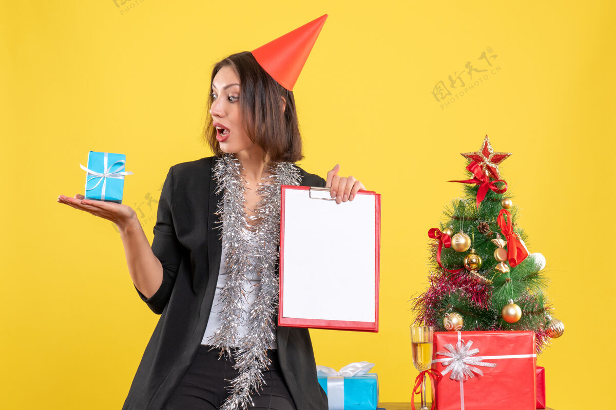 时尚圣诞心情与惊喜美丽的女士手持文件和礼物在黄色的办公室人黄色圣诞节
