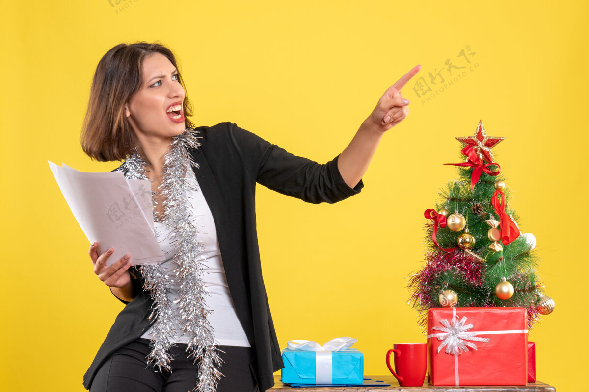 微笑圣诞节心情与情绪紧张的美丽女士站在办公室里 拿着文件在办公室里的黄色新郎快乐情绪