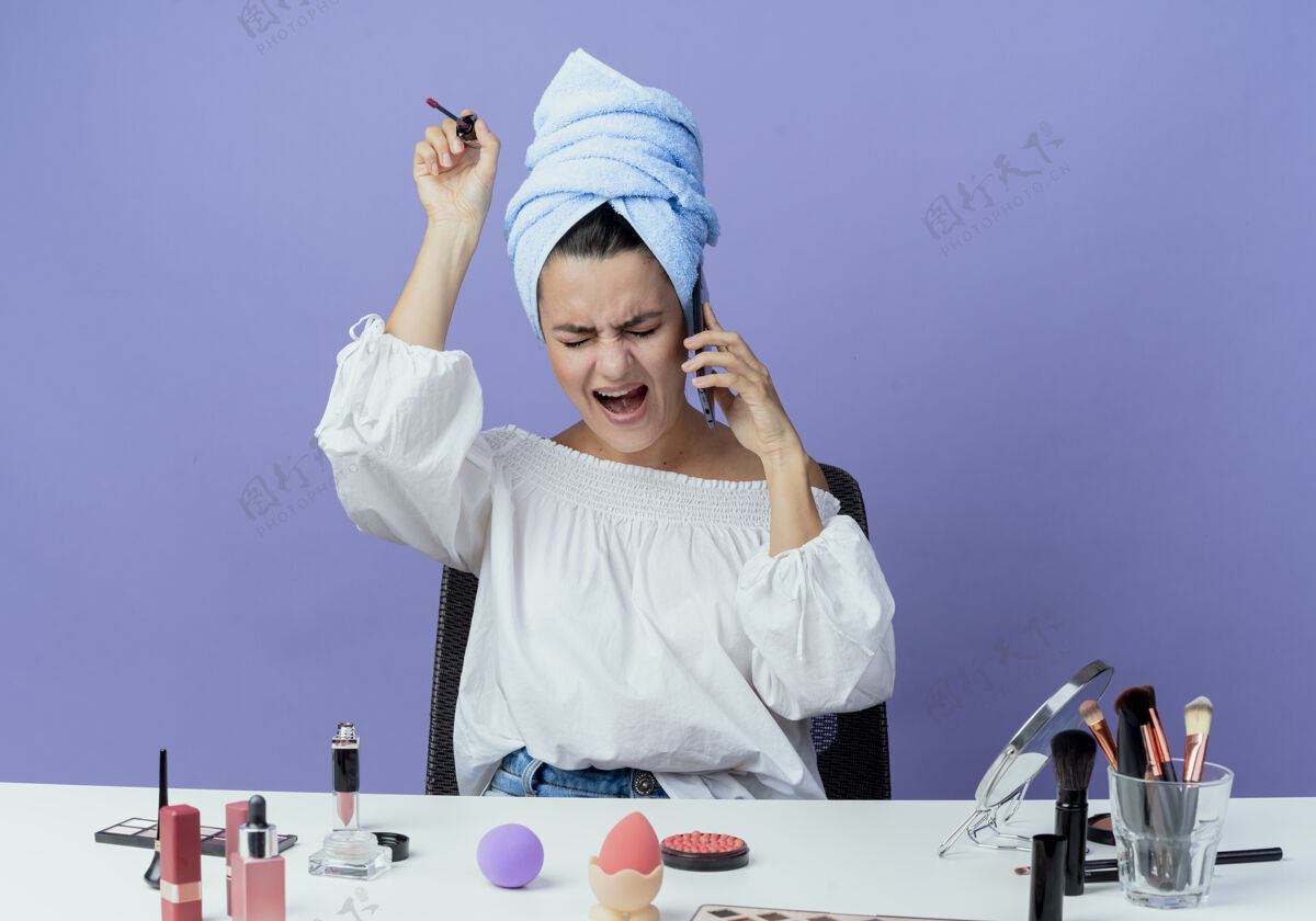 漂亮恼人的漂亮女孩裹着发巾坐在桌子上用化妆工具喊着拿着唇彩在电话上对着紫墙隔绝电话毛巾嘴唇电话