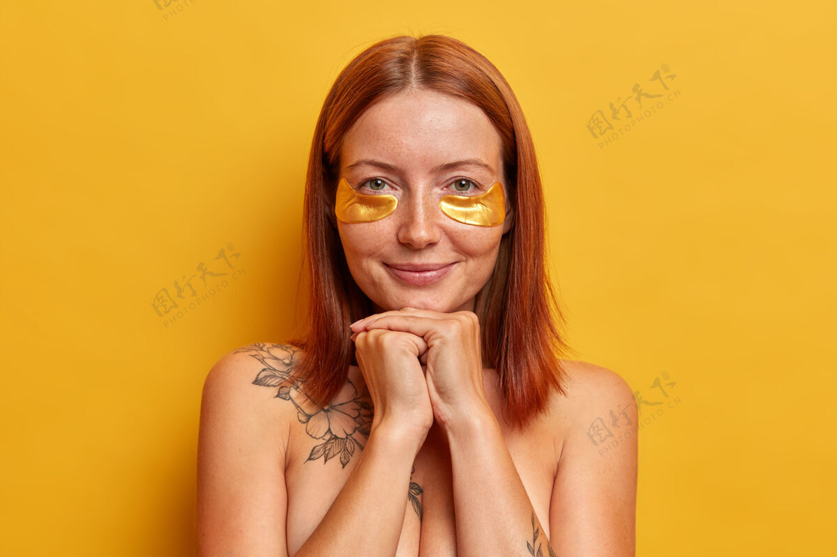 完美红发美女bob发型头像 享受美容程序 贴胶原蛋白金色贴片 裸体站在室内 关心皮肤和外表 隔离在黄色墙壁上治疗柔软室内