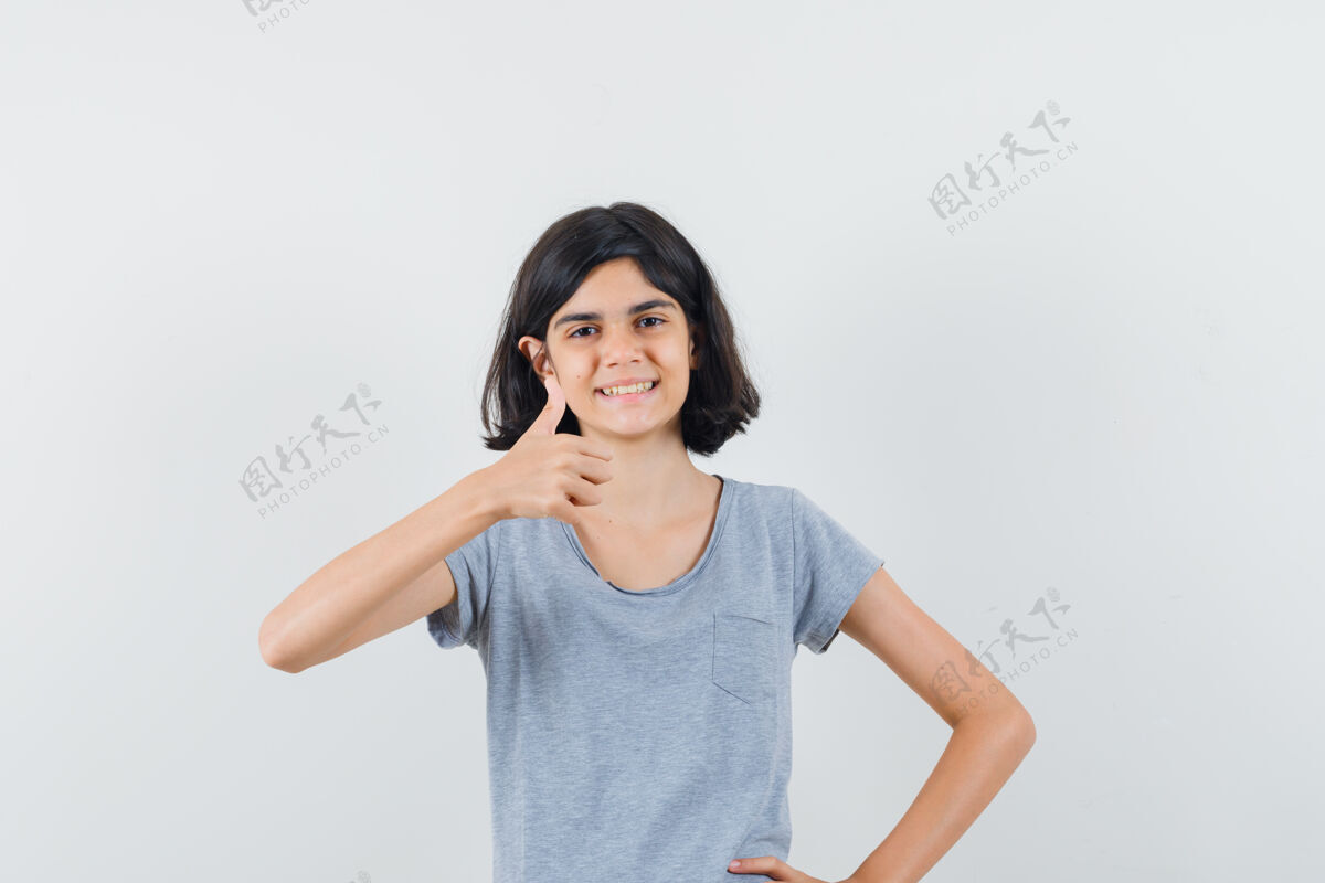 微笑穿着t恤衫的小女孩竖起大拇指 看起来很高兴 正面视图人肖像小