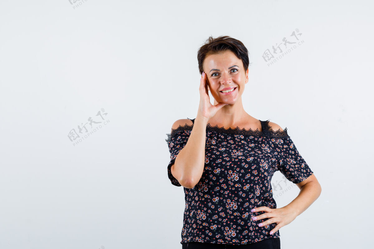 活跃成熟的女人面颊靠在手掌上 手放在腰上 穿着花衬衫 黑色的裙子 看起来很自信 前视商务老年人脸颊