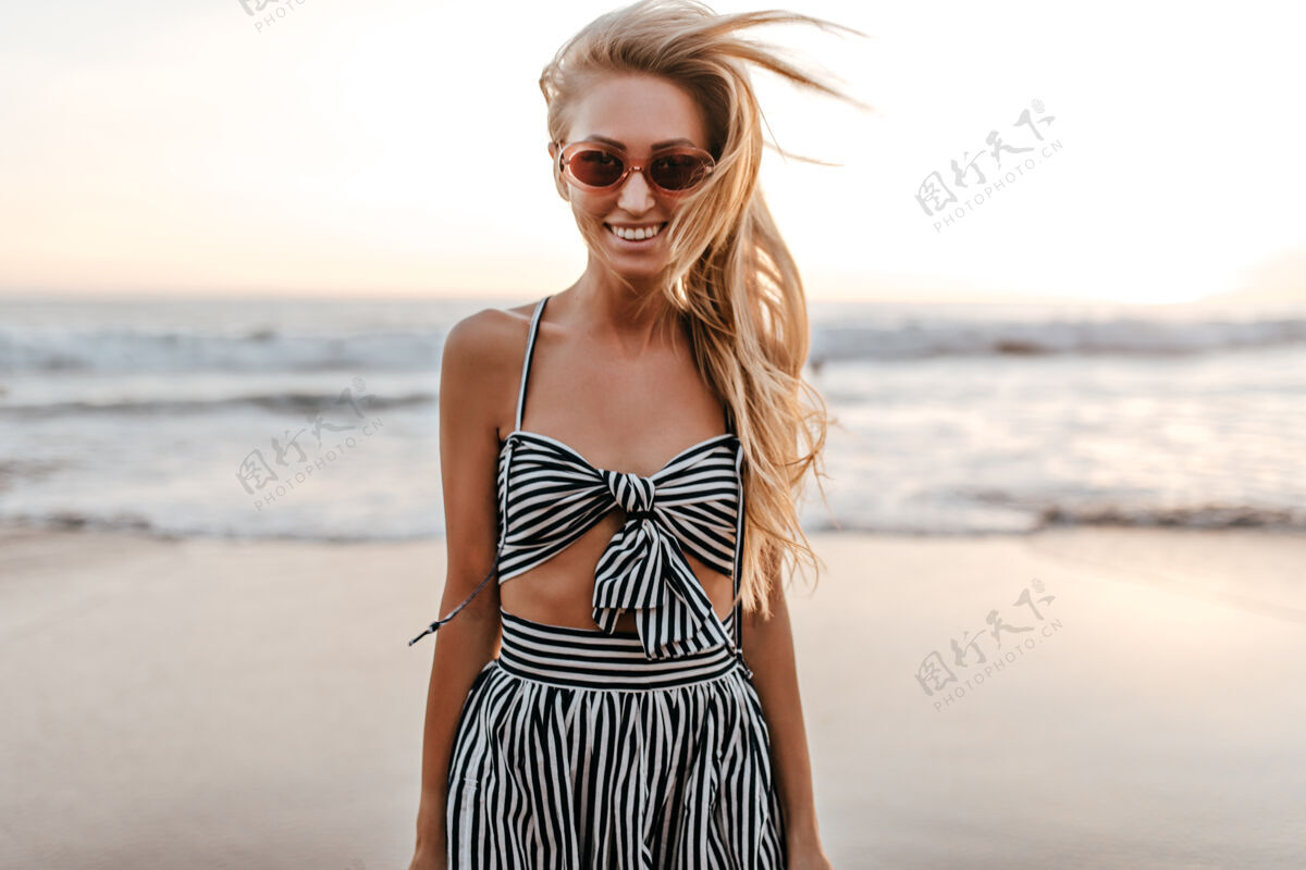 漂亮穿着条纹不规则上衣和裙子的酷酷活跃的女人在海边真诚地微笑年轻优雅头发