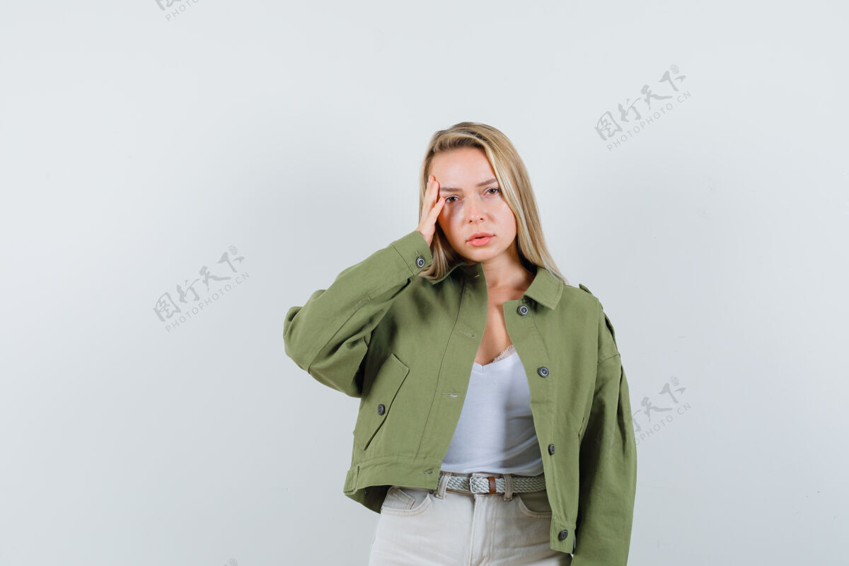 肖像年轻的女士手拉着太阳穴 穿着夹克 裤子 看上去心烦意乱 前视不清女孩漂亮夹克