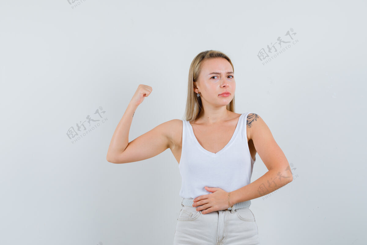 女孩金发女士展示手臂肌肉在单打 裤子和看起来自信前视图手臂秀漂亮