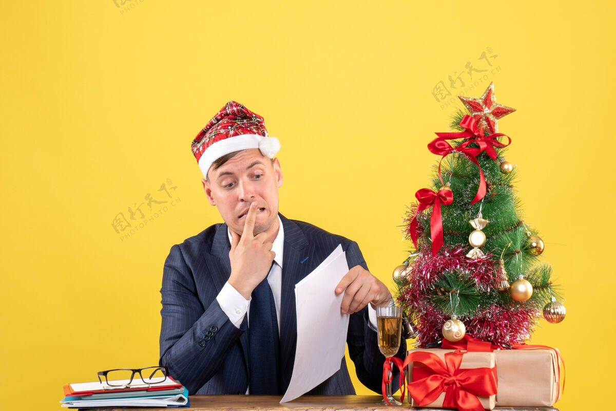 办公室前视图激动的男子坐在圣诞树附近的桌子上 呈现黄色背景商务树附近