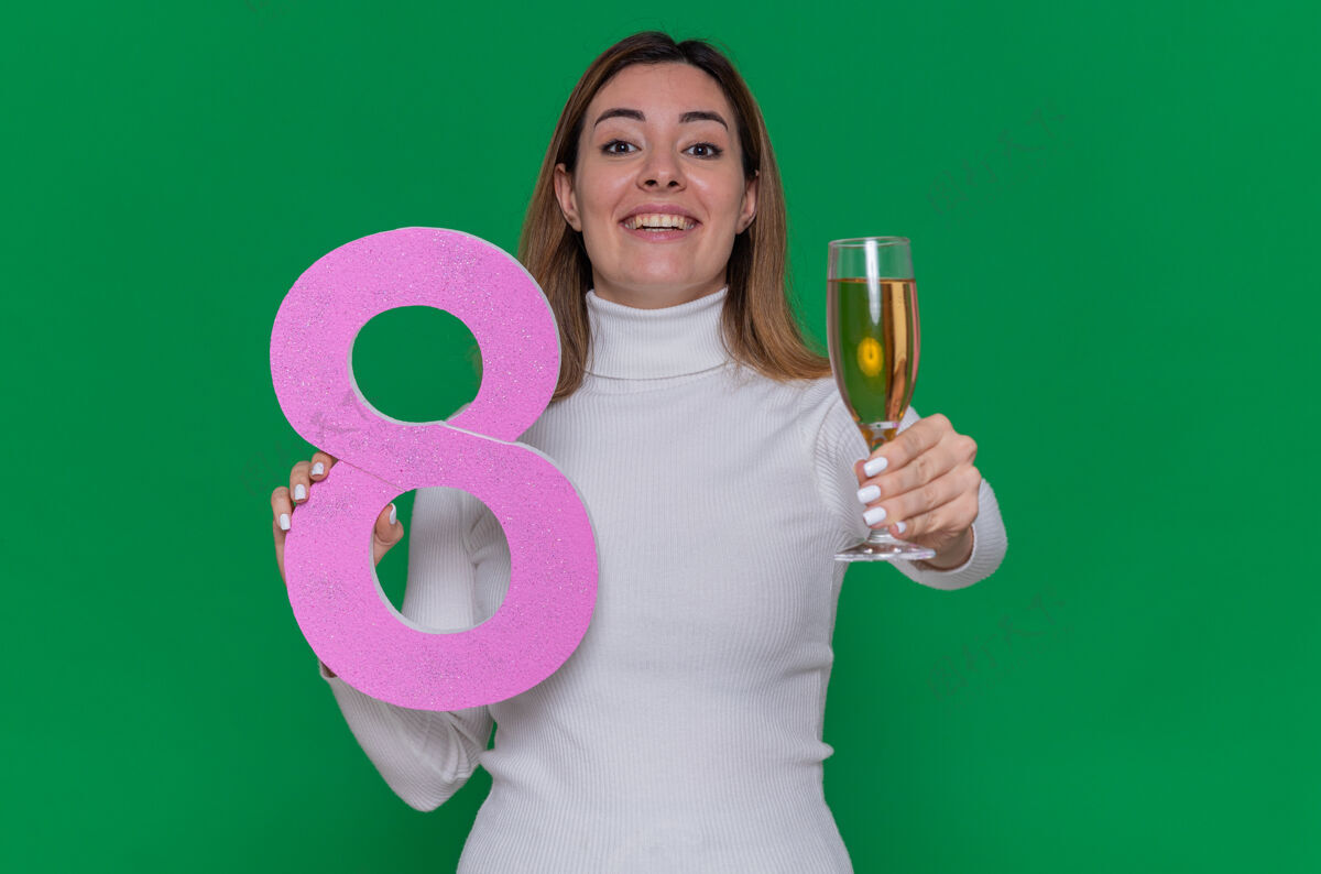 快乐穿着白色高领毛衣 拿着8号和一杯香槟的快乐年轻女子三月欢呼香槟