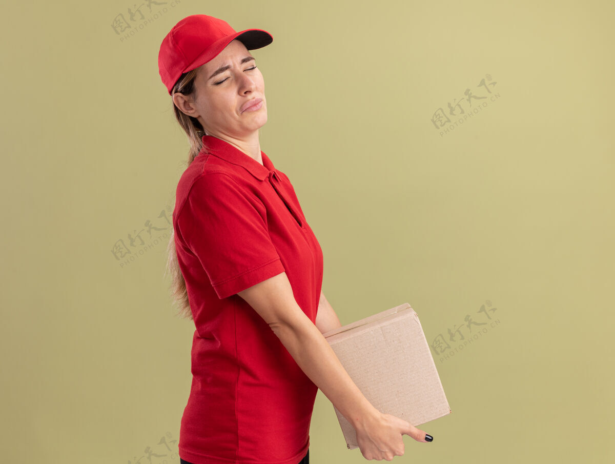 感情一个穿着制服的悲伤的年轻漂亮的女送货员站在一边 手里拿着橄榄绿墙上的名片盒年轻立场表情