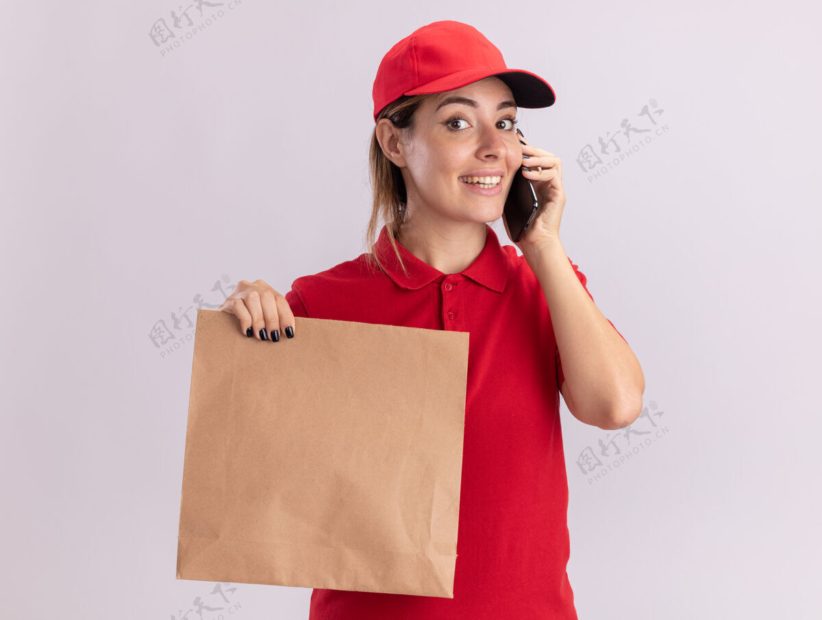 站着身着制服 面带微笑的年轻漂亮女送货员拿着纸包 隔着白墙讲电话表情微笑人